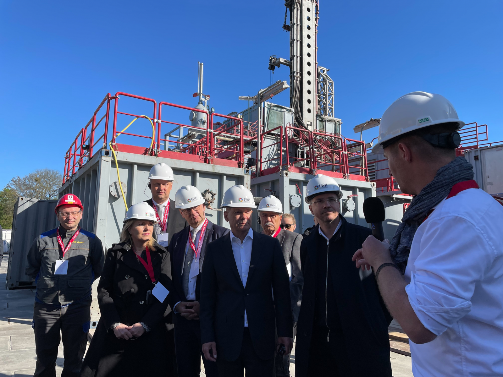 Bundeskanzler MdB Olaf Scholz (5.v.l.) und Oberbürgermeister Mike Schubert (2.v.r.) zu Besuch an der Tiefengeothermie der EWP. Tristan Grüttner, Projektleiter EWP, (rechts mit Mikro), erläutert die Technik.  v.l.n.r.: Andreas Brecht (Geschäftsführer Diens