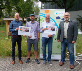 Christian Hoffmann (links), Leiter Abteilung Kunde & Öffentlichkeit der Mainzer Mobilität und Olaf Nehrbaß (rechts), Amtsleiter Grün- und Umweltamt (rechts) übergeben die beiden Hauptgewinne im Fotowettbewerb Klimaschutz und Klimawandel an den Erstplatzie