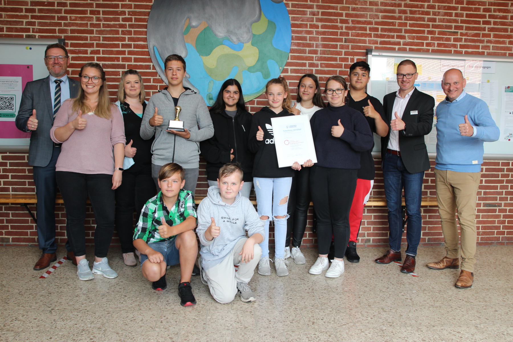 Foto ©Landkreis Harburg / Bildunterschrift:  Die Schülerinnen und Schüler und Lehrkräfte sowie Schulleiter Andreas Neises (rechts) freuen sich über die „Goldene Glühbirne“, den ersten Preis im Wettbewerb „Dreh Ab!“, den Kreisrat Josef Nießen (links) und K