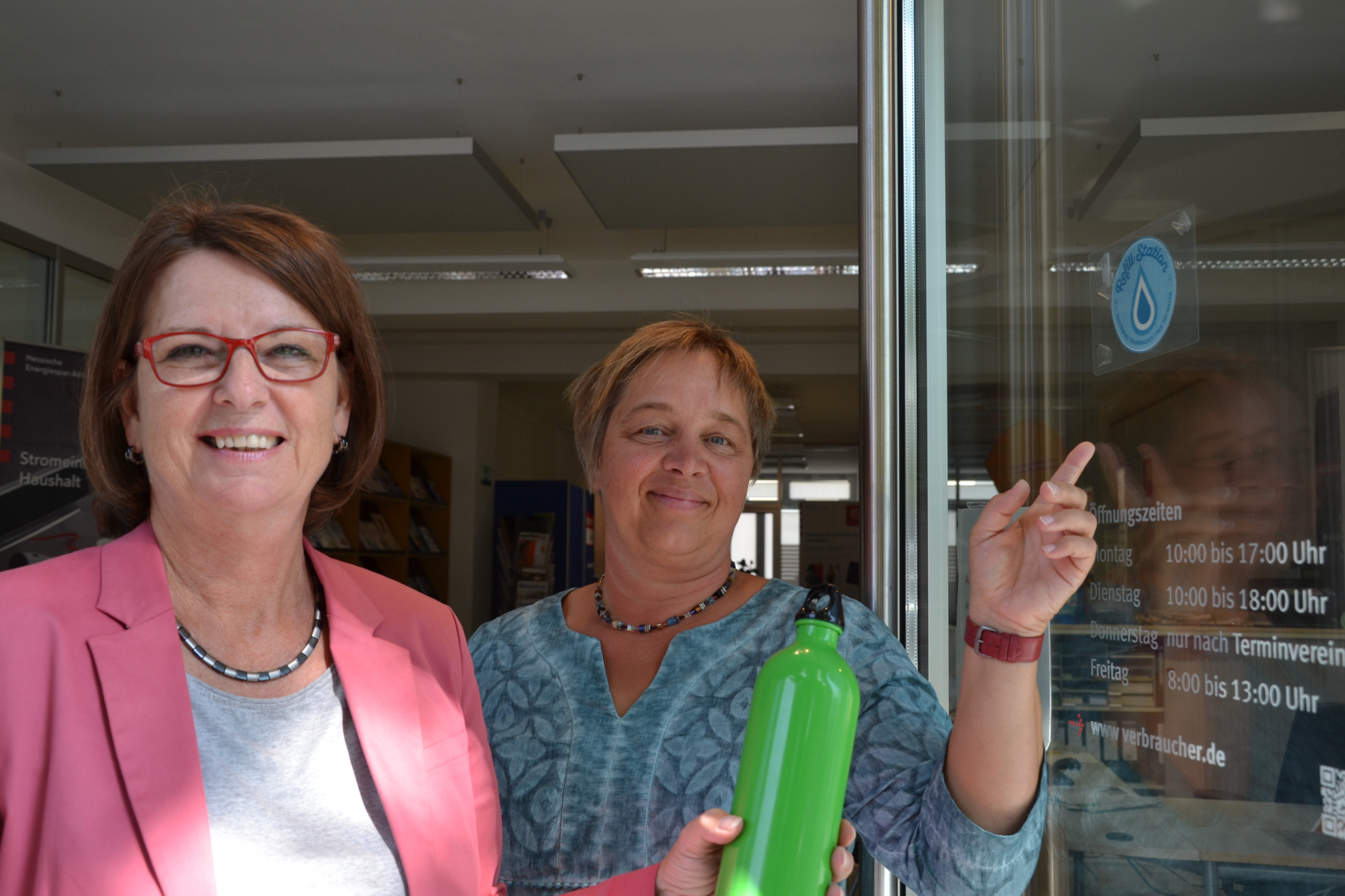 Foto von Ministerin Priska Hinz gemeinsam mit Aria van Dijk, Beraterin der Verbraucherzentral, beim Anbringen des Refill-Aufklebers an der Verbraucherzentrale in Wiesbaden.